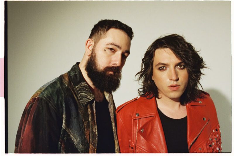 Loveless Press Photo. Two band members photographed from the chest up, one wearing a black leather jacket and the other wearing a red leather jacket
